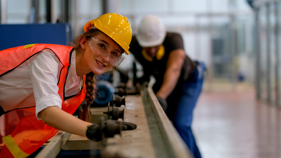 Worker or technician or engineer woman smile and look forward in front of rail of the machine with her co-worker as background in factory.
